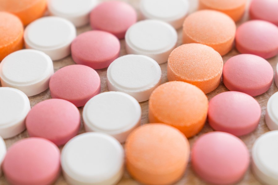 Różowe, pomarańczowe i białe tabletki ułożone w rzędach.