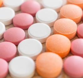 Różowe, pomarańczowe i białe tabletki ułożone w rzędach.