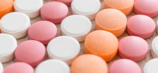 Różowe, pomarańczowe i białe tabletki ułożone w rzędach.