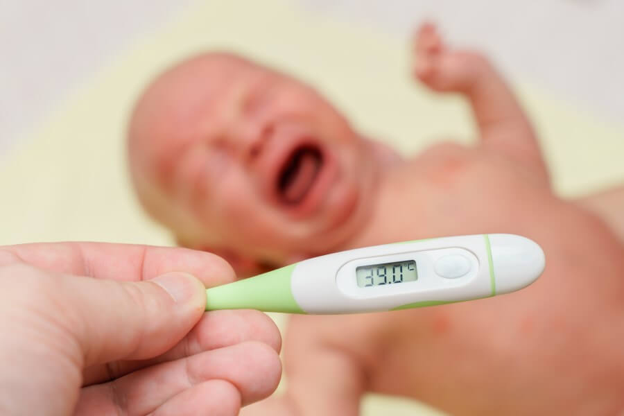 Rodzic mierzy temperaturę u płaczącego noworodka.