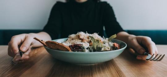 Głodna kobieta siedzi przed talerzem pysznej sałatki. Za uczucie głodu odpowiada hormon grelina.