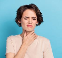 Kobieta trzyma się za szyje, odczuwa ból gardła powodowany grzybiczym zapaleniem gardła.