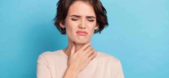 Kobieta trzyma się za szyje, odczuwa ból gardła powodowany grzybiczym zapaleniem gardła.