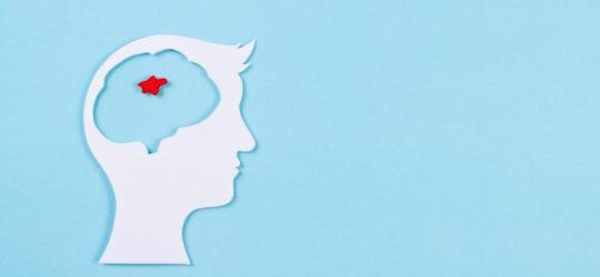 Wycięta z papieru głowa człowieka. W obszarze mózgu zaznaczony na czerwono guz mózgu.