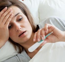 Kobieta leży w łóżku i mierzy sobie temperaturę. Ma gorączkę i zastanawia się, ile trwa grypa?