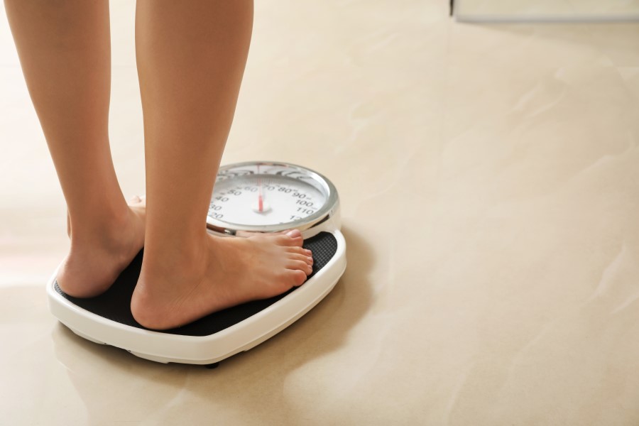Kobieta stoi na wadze. Lęk przed przyrostem masy ciała to jeden z objawów anoreksji.