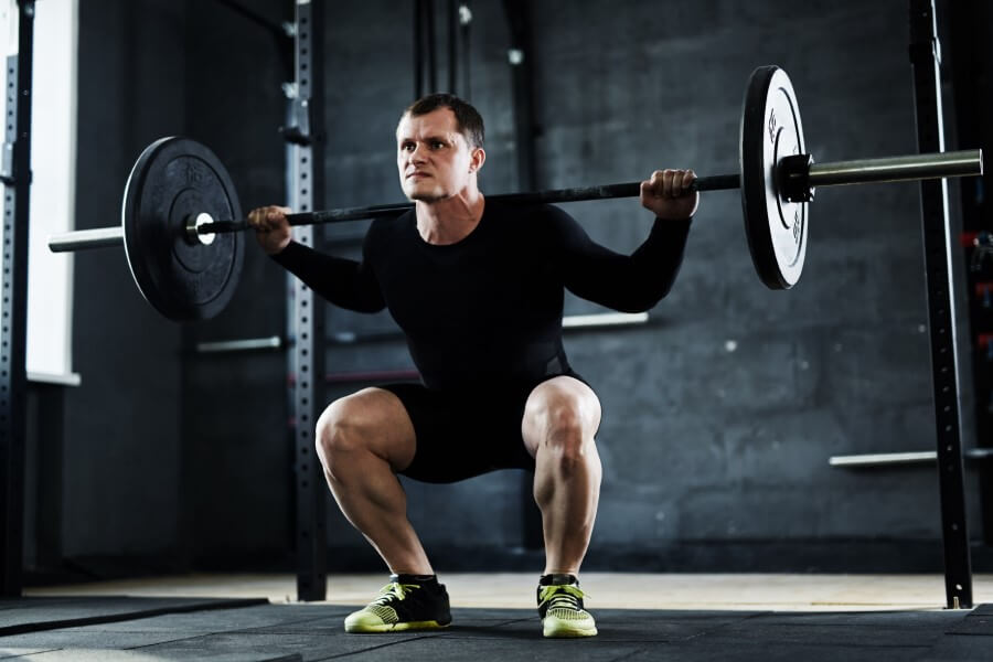 Mężczyzna podczas treningu siłowego, wykonuje przysiad ze sztangą.