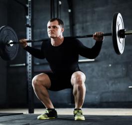 Mężczyzna podczas treningu siłowego, wykonuje przysiad ze sztangą.