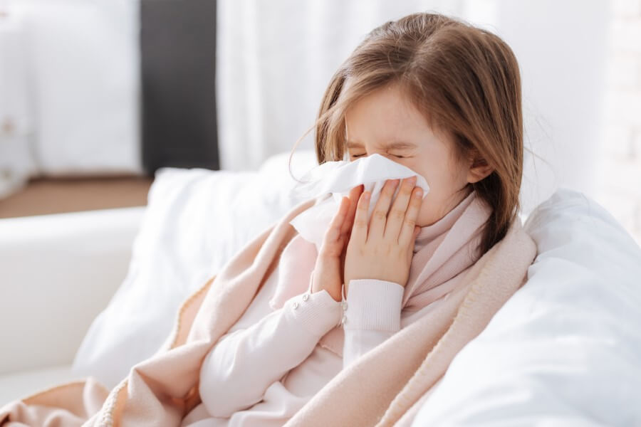 Przeziębiona dziewczynka wydmuchuje nos.