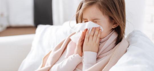 Przeziębiona dziewczynka wydmuchuje nos.
