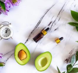 Kosmetyki, awokado, zegarek i kwiaty na marmurowym blacie.