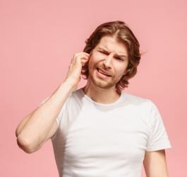 Różowe tło. Mężczyzna próbuje odetkać bolesne, zatkane ucho.