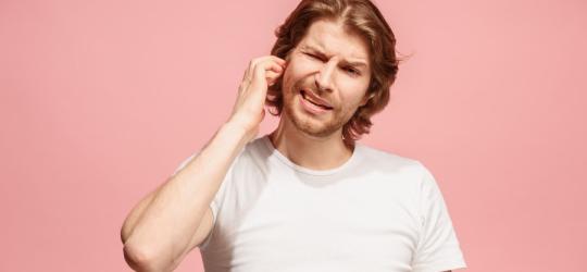 Różowe tło. Mężczyzna próbuje odetkać bolesne, zatkane ucho.