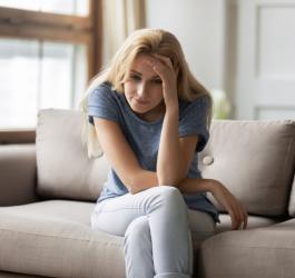 Zmęczona kobieta siedzi na kanapie, opiera rękę o głowę.