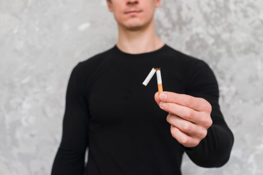Mężczyzna rzuca palenie, trzyma w dłoni przełamanego papierosa.