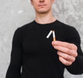 Mężczyzna rzuca palenie, trzyma w dłoni przełamanego papierosa.