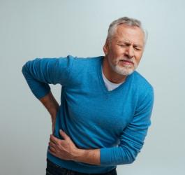 Mężczyzna trzyma się za plecy, dokuczają mu objawy kamicy nerkowej.