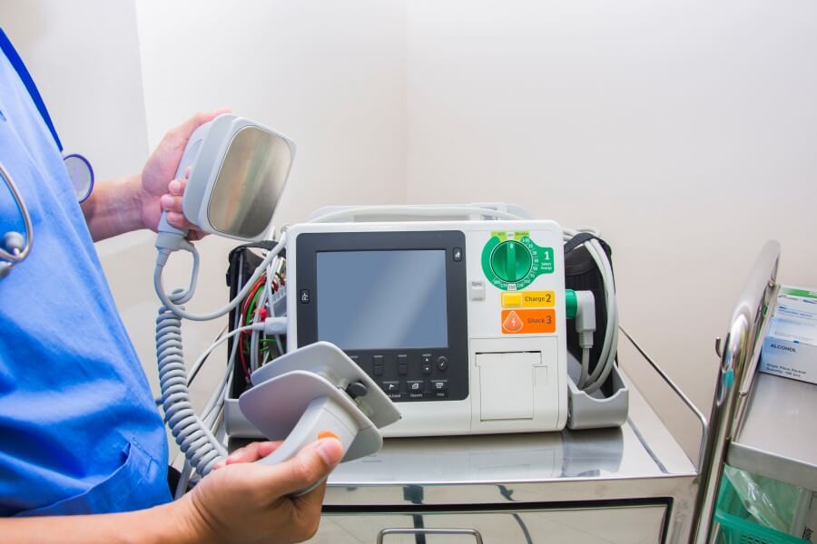 Lekarz trzyma w rękach defibrylator, którym wykonuje się kardiowersję elektryczną.