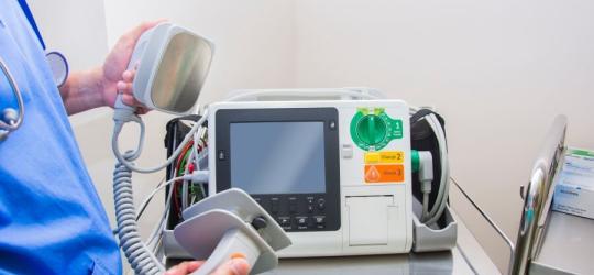 Lekarz trzyma w rękach defibrylator, którym wykonuje się kardiowersję elektryczną.