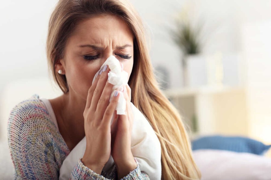 Kobieta jest przeziębiona, ma katar, wydmuchuje nos w chusteczkę higieniczną. 