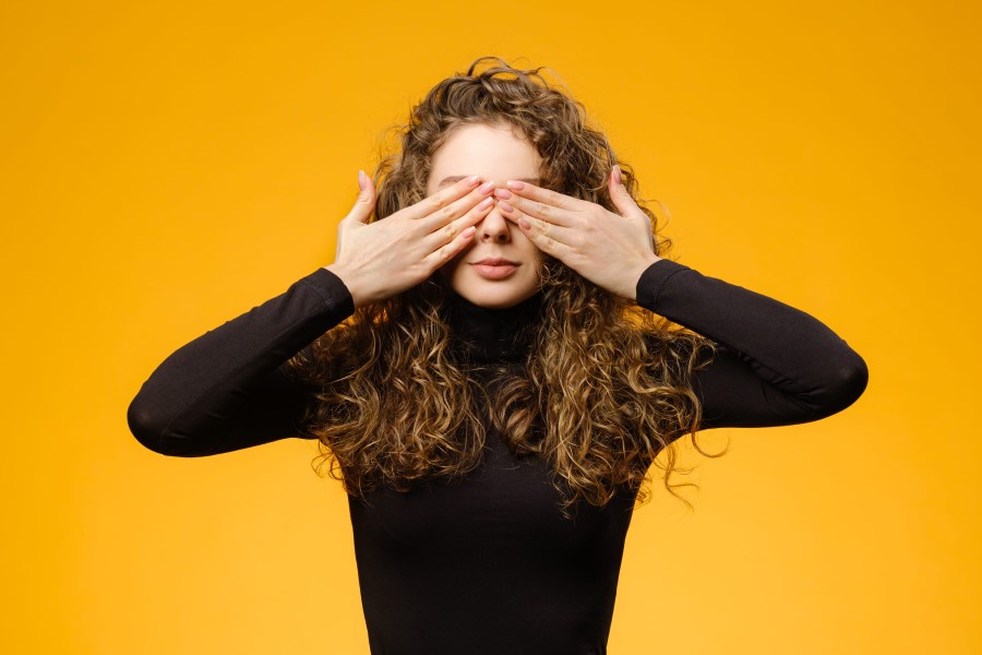 Kobieta w kręconych włosach zasłania dłońmi swoje oczy.