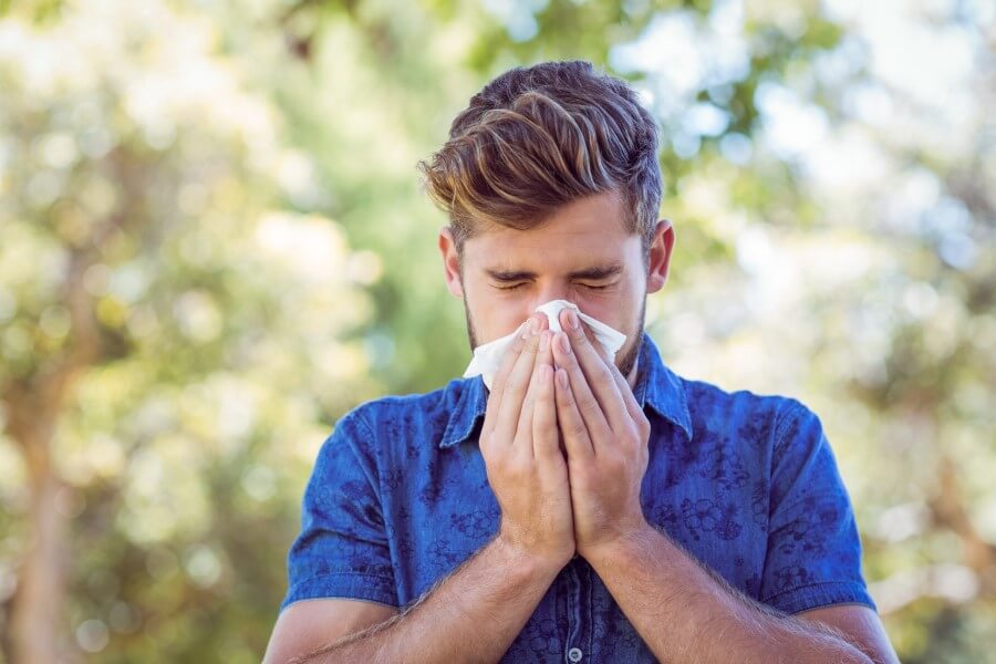 Mężczyzna wydmuchuje nos, jest uczulony na pyłki roślin i cierpli z powodu objawów alergii.