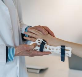 Lekarz zakłada pacjentce ortezę na rękę.
