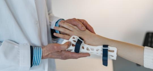 Lekarz zakłada pacjentce ortezę na rękę.