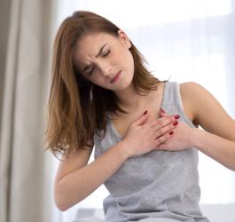 Młoda kobieta chwyta się za klatkę piersiową, odczuwa niepokojące kłucie serca