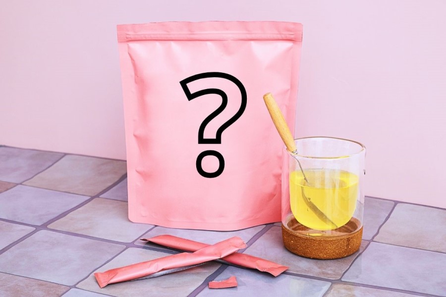 Różowa torebka, saszetki oraz szklanka zawierająca rozpuszczony kolagen.