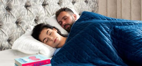 Kobieta i mężczyzna śpią w łóżku, leżą pod kołdrą obciążeniową.