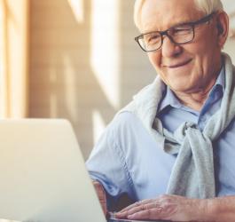 Starszy mężczyzna w okularach korzysta ze swojego laptopa.