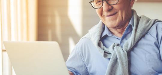 Starszy mężczyzna w okularach korzysta ze swojego laptopa.