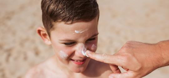 Rodzic smaruje chłopczyka kremem z filtrem przeciwsłonecznym.