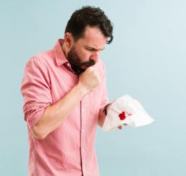 Mężczyzna, u którego wystąpiło krwioplucie po kaszlu. Widać ślady krwi na chusteczce higienicznej.