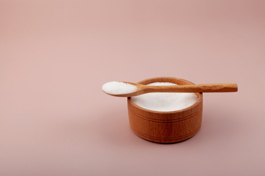 Drewniana miseczka wypełniona ksylitolem, na niej łyżeczka również wypełniona ksylitolem.