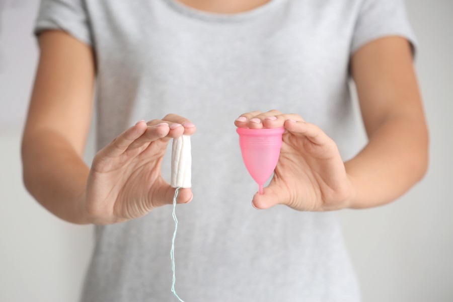 Kobieta trzyma w jednej dłoni tampon, a w drugiej kubeczek menstruacyjny.