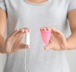 Kobieta trzyma w jednej dłoni tampon, a w drugiej kubeczek menstruacyjny.