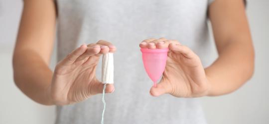 Kobieta trzyma w jednej dłoni tampon, a w drugiej kubeczek menstruacyjny.