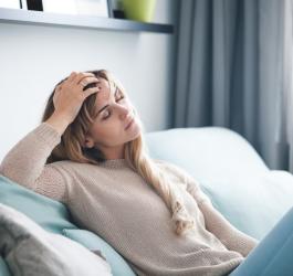 Kobieta siedzi na kanapie, jest osłabiona i zmęczona.