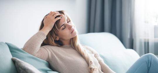 Kobieta siedzi na kanapie, jest osłabiona i zmęczona.