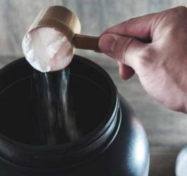 Mężczyzna przy pomocy miarki nabiera porcję suplementu z opakowania zbiorczego.