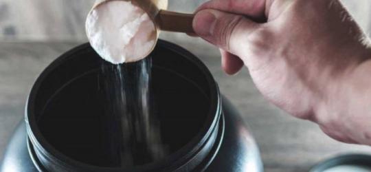 Mężczyzna przy pomocy miarki nabiera porcję suplementu z opakowania zbiorczego.