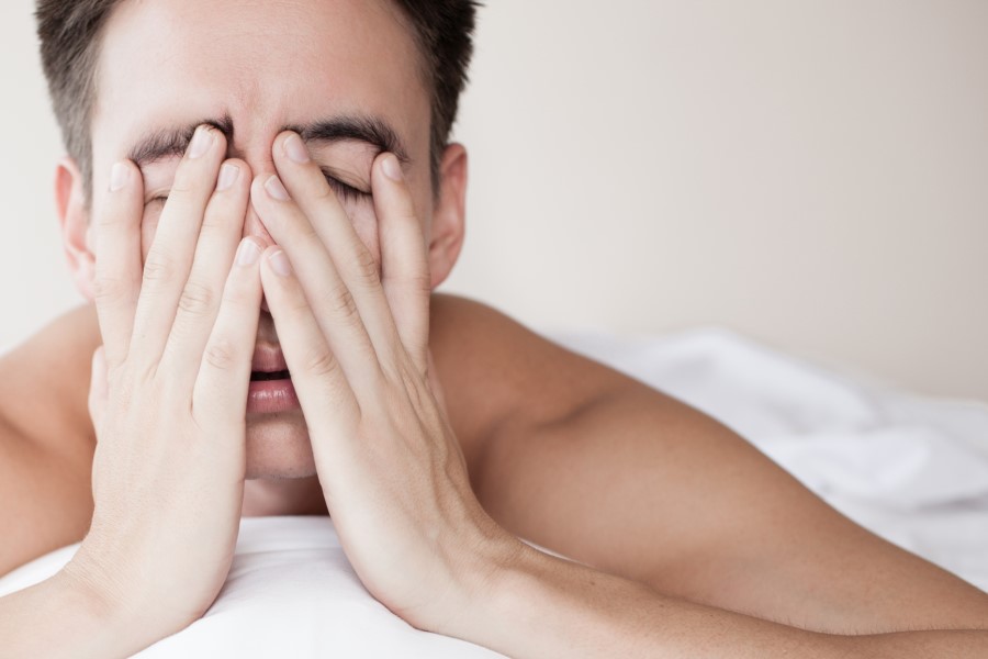 Zmęczony, niewyspany mężczyzna leży w łóżku.