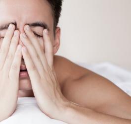 Zmęczony, niewyspany mężczyzna leży w łóżku.