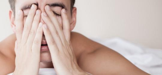 Zmęczony, niewyspany mężczyzna leży w łóżku.