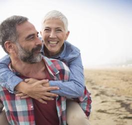 Dorosła, zakochana para na plaży. Mężczyzna niesie na barana swoją partnerkę.