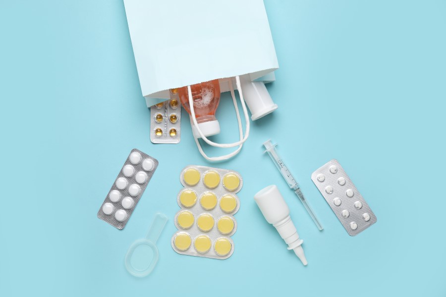 Blistry leków, syrop, aerozol i zastrzyk wysypane z torebki na zakupy.