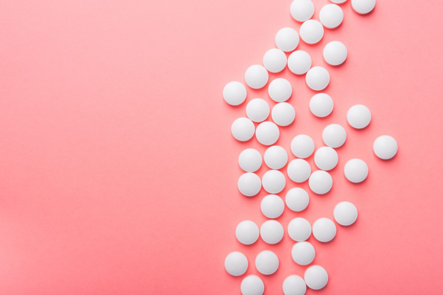 Białe tabletki na różowym tle.