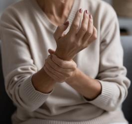 Kobieta trzyma się za rękę, odczuwa ból stawów.